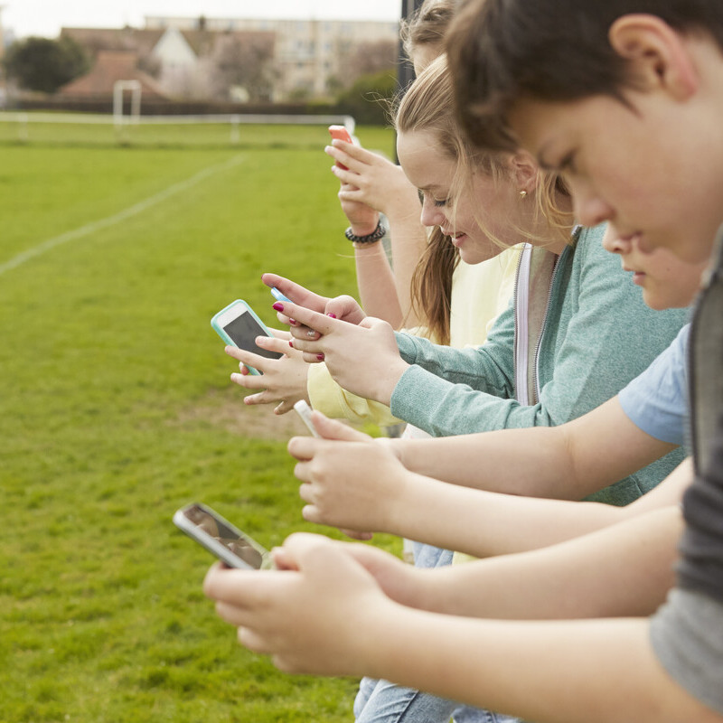 Row of five boys and girls reading smartphone text messages at football pitch